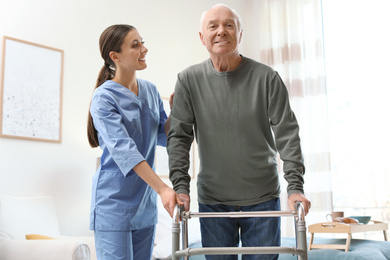 Photo of Care worker helping elderly man with walker in geriatric hospice