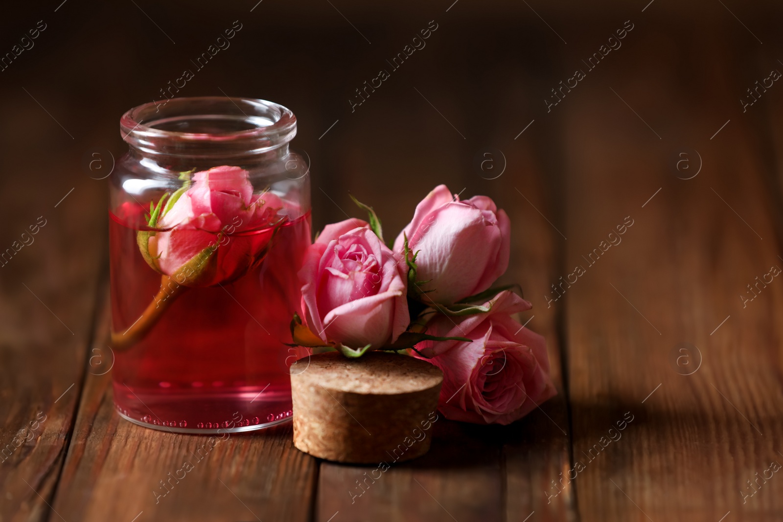 Photo of Bottle of essential rose oil and flowers on wooden table