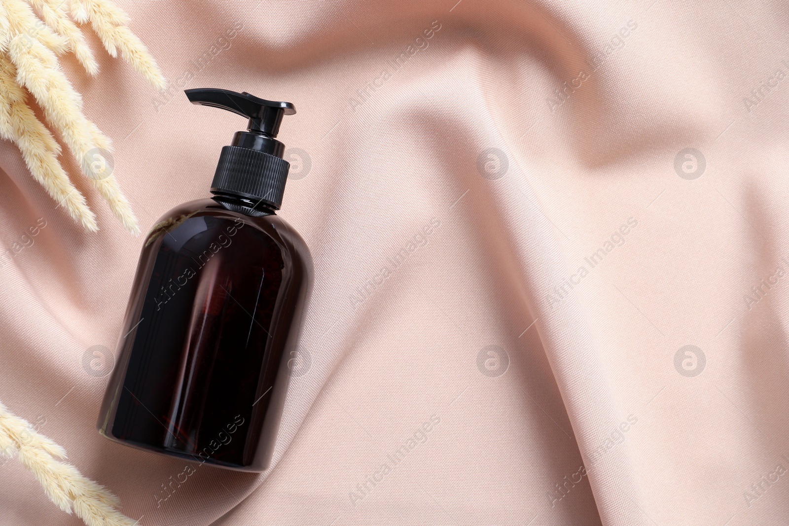 Photo of Bottle of cosmetic product and dry spikes on pink fabric, flat lay. Space for text