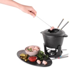 Woman dipping piece of raw meat into oil in fondue pot on white background