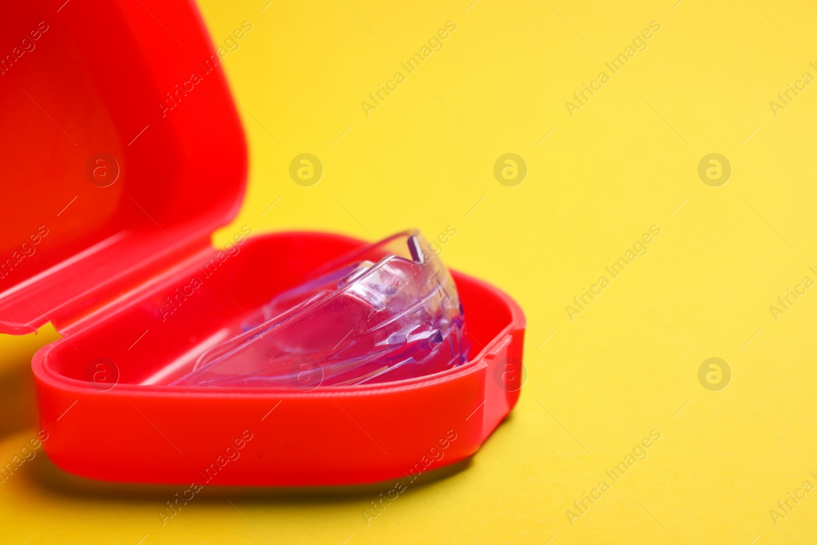 Photo of Bite correction. Container with dental mouth guard on yellow background, closeup. Space for text