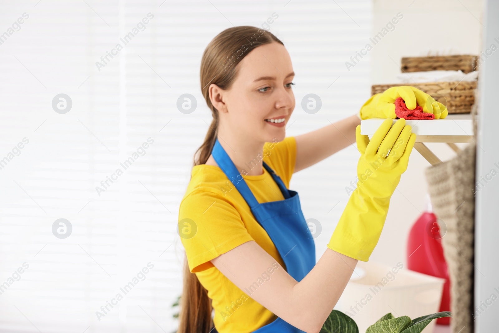 Photo of Woman cleaning shelf with rag at home, space for text