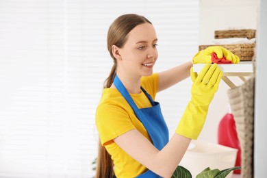 Woman cleaning shelf with rag at home, space for text