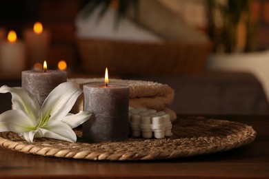 Photo of Spa composition with burning candles, lily flower and towels on wooden table in wellness center, space for text