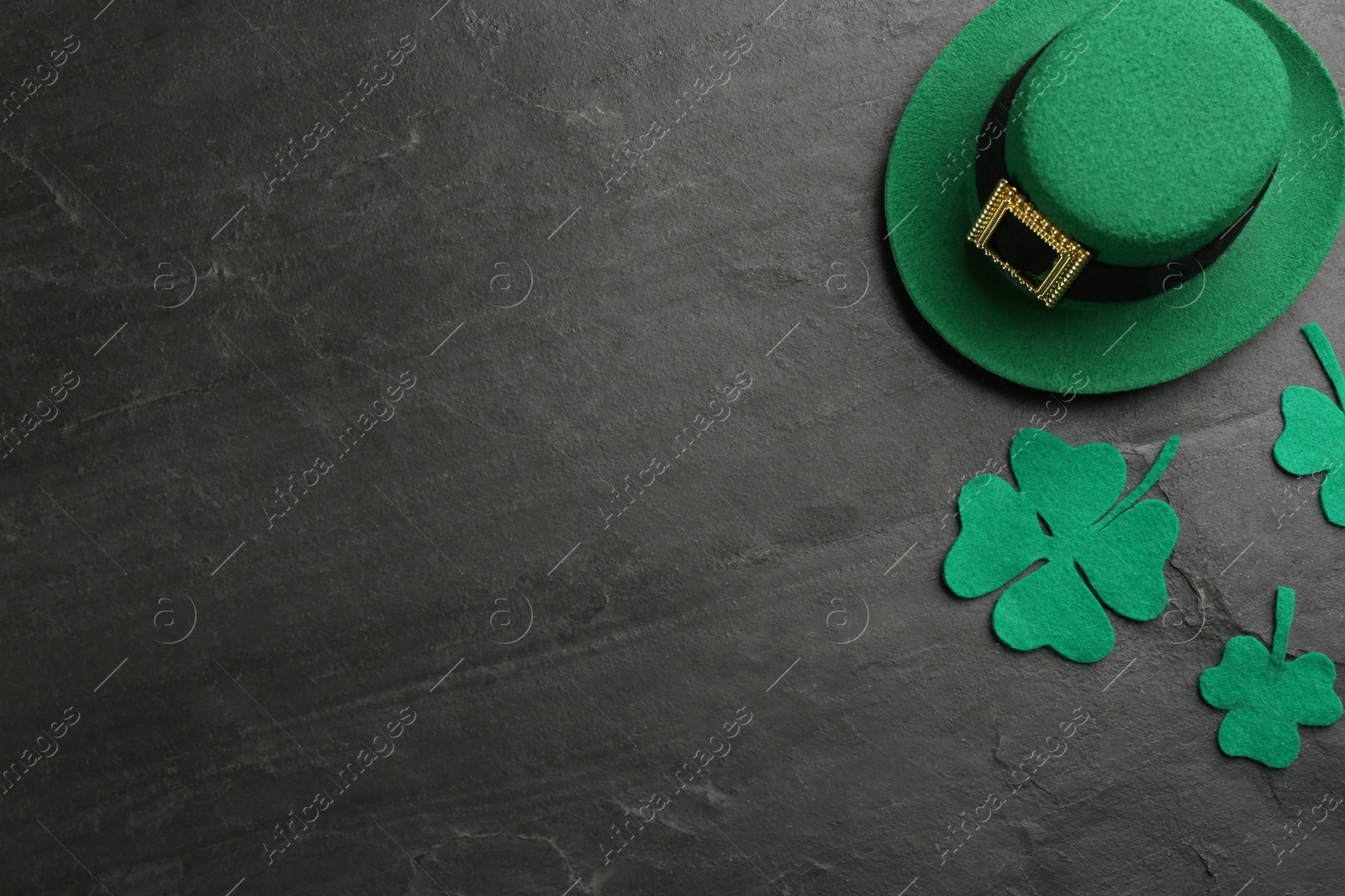 Photo of Leprechaun's hat and decorative clover leaves on black background, flat lay with space for text. St. Patrick's day celebration