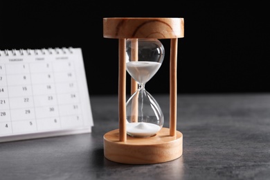 Photo of Hourglass and calendar on table against black background. Time management