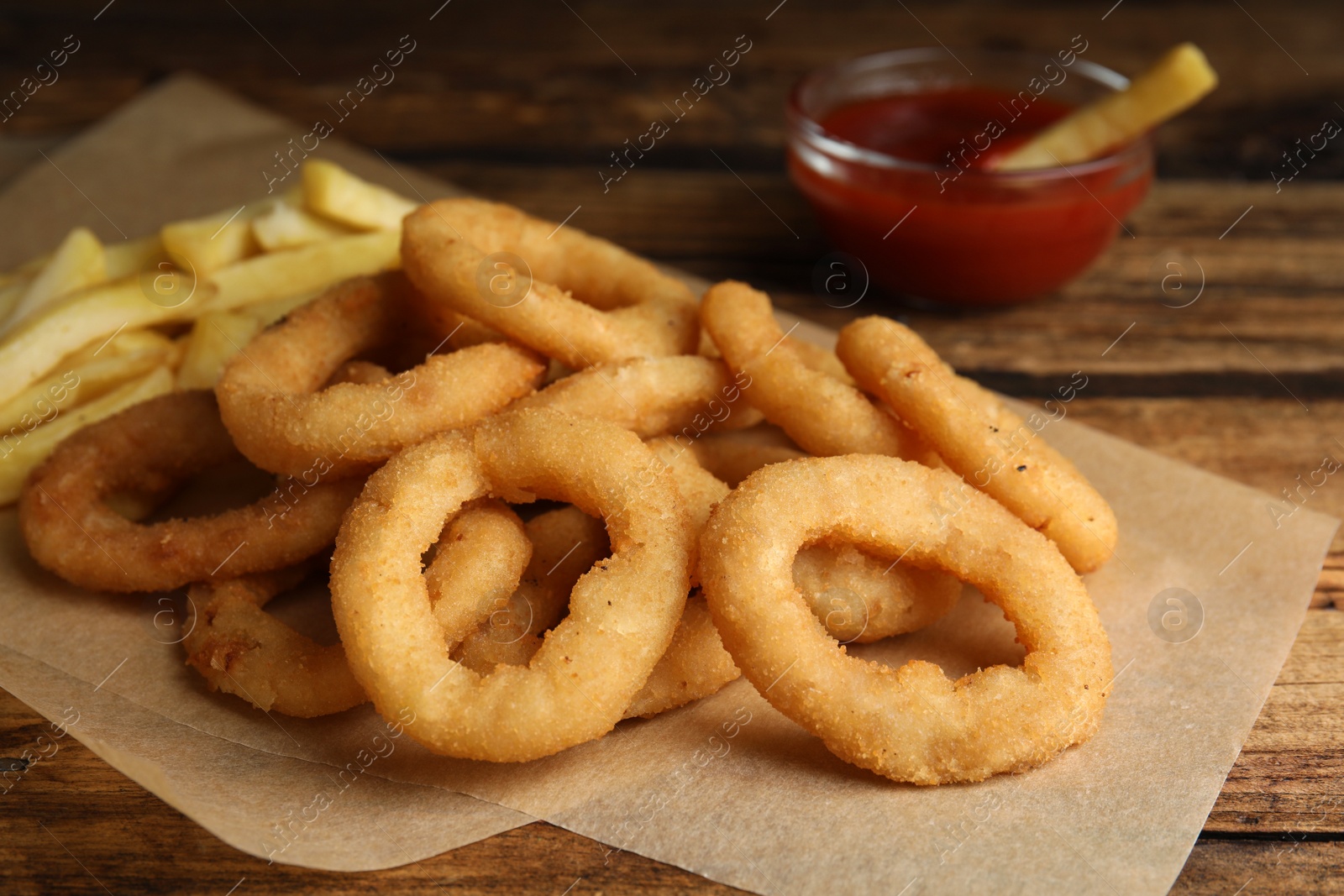 Photo of Delicious onion rings, fries and ketchup on wooden table, closeup