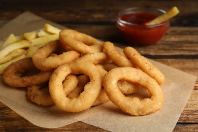Delicious onion rings, fries and ketchup on wooden table, closeup