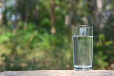 Glass of water on wooden surface outdoors, space for text