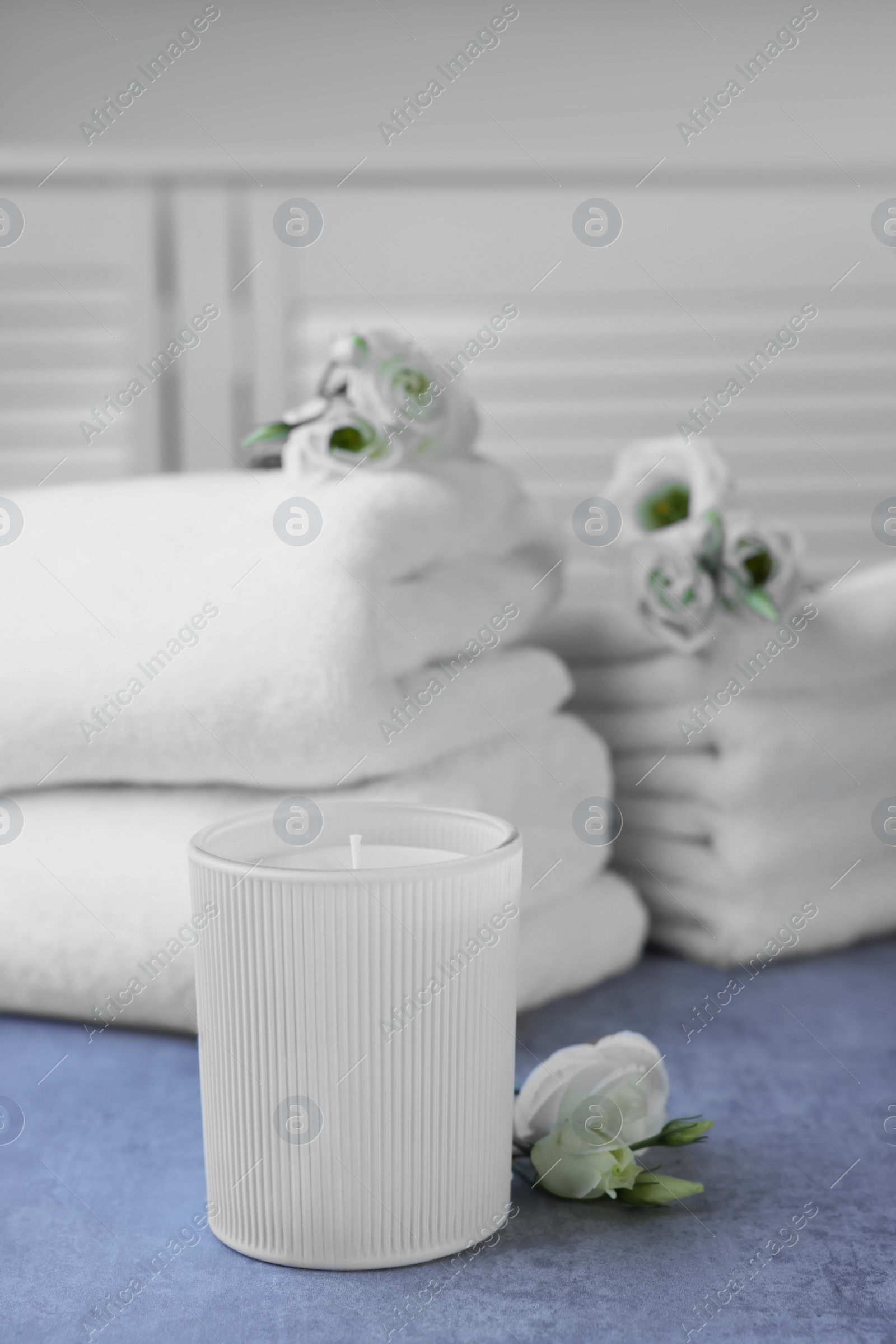 Photo of Scented candle, folded towels and eustoma flowers on gray marble table