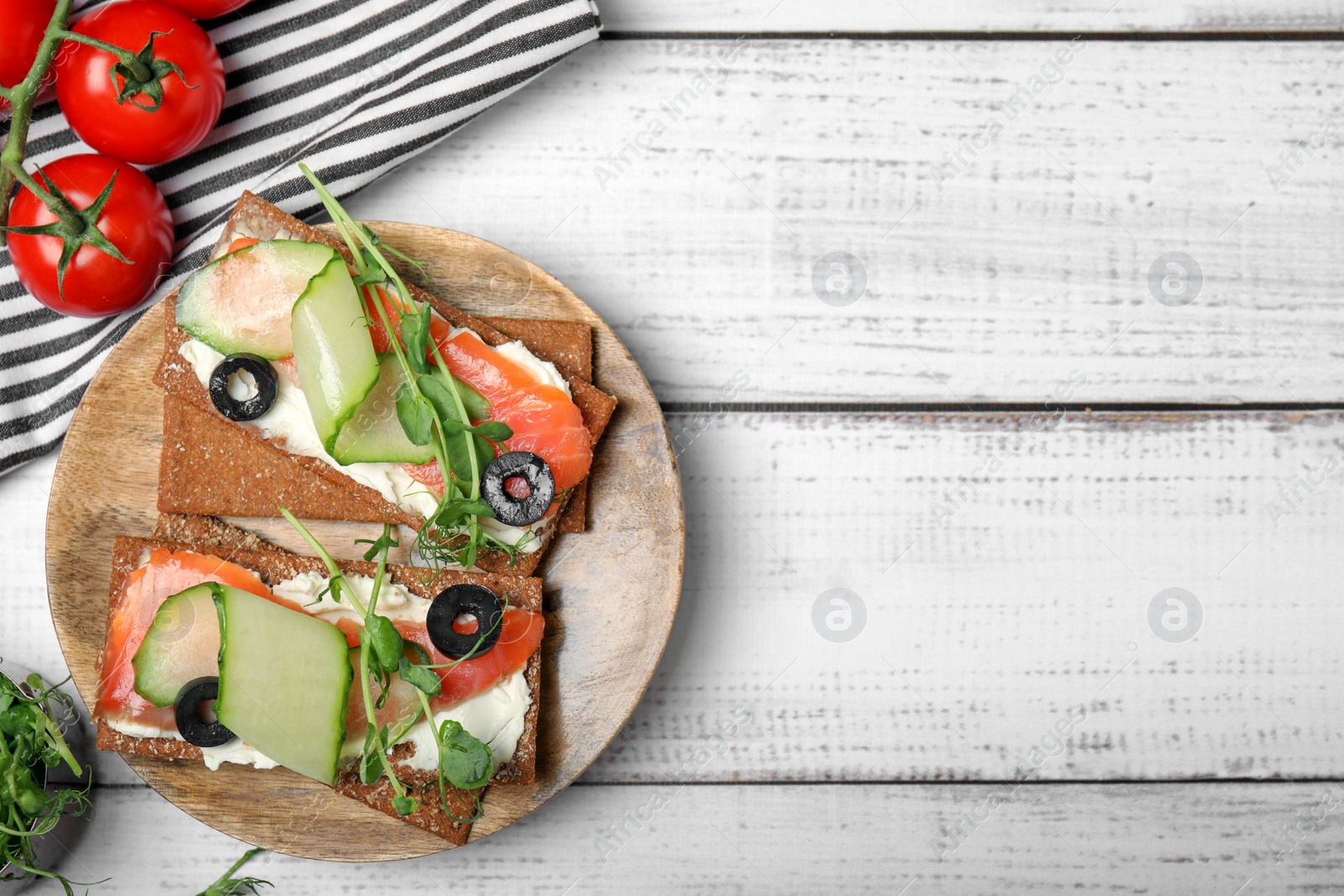 Photo of Tasty rye crispbreads with salmon, cream cheese and vegetables on white wooden table, flat lay. Space for text