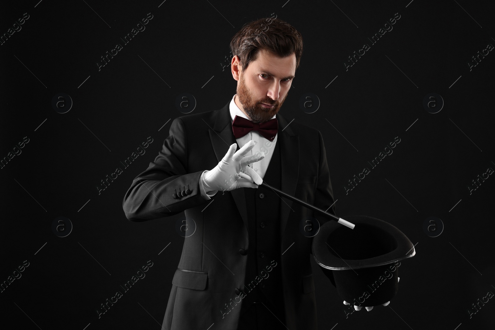 Photo of Magician showing magic trick with top hat on black background