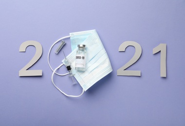 Photo of Paper numbers, medical mask, vial and syringe forming 2021 on violet background, flat lay. Coronavirus vaccination