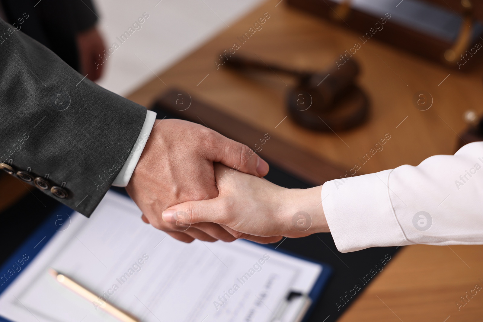 Photo of Notary shaking hands with client at wooden table in office, closeup