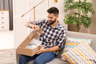 Photo of Young man opening parcel on sofa at home