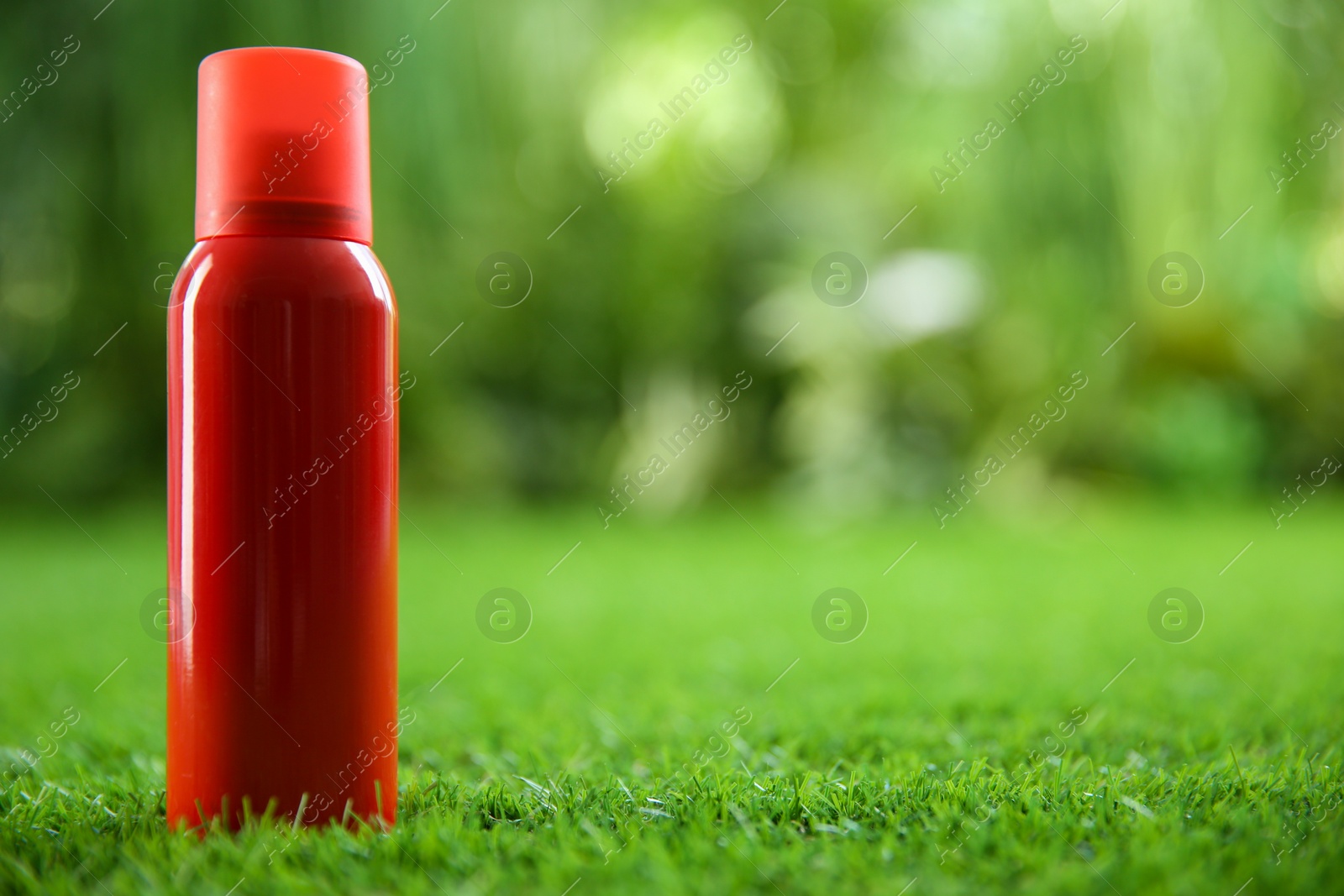 Photo of Bottle of insect repellent spray on green grass. Space for text