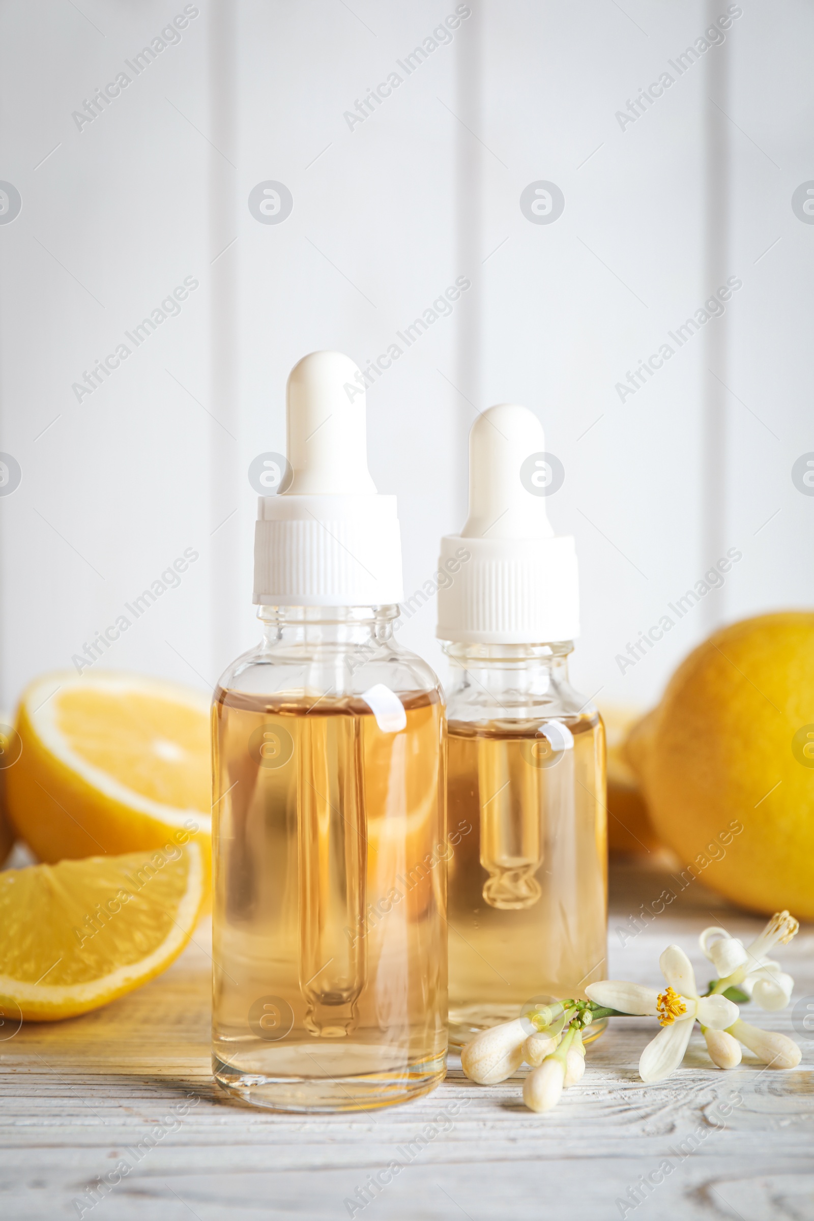 Photo of Bottles of citrus essential oil, flower and lemons on white wooden table