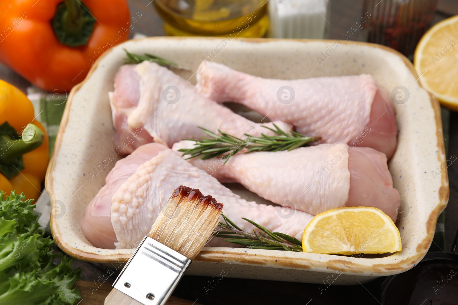 Photo of Basting brush with marinade, raw chicken drumsticks, rosemary and lemon on table, closeup