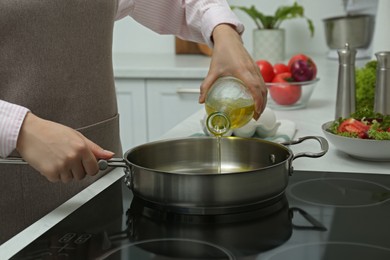 Woman pouring oil from jug into pan in kitchen, closeup