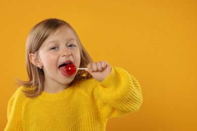 Photo of Portrait of happy girl licking lollipop on orange background, space for text