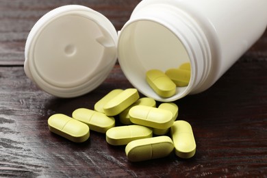 Photo of Bottle and vitamin pills on wooden table, closeup