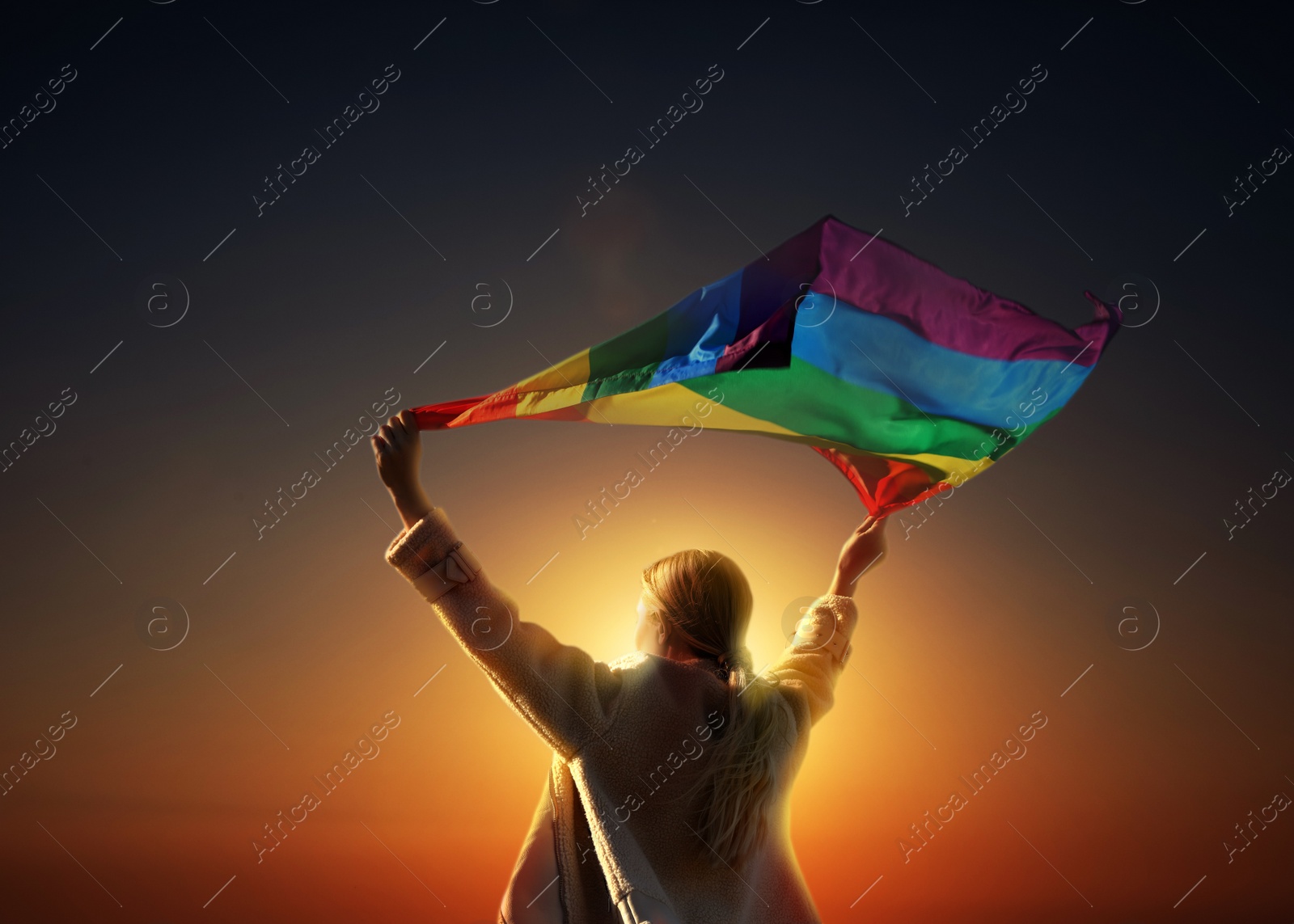 Image of Woman with bright LGBT flag against sky at sunset