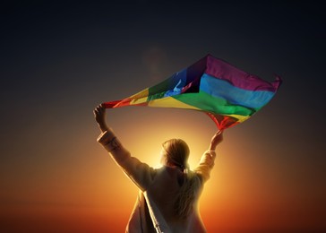 Image of Woman with bright LGBT flag against sky at sunset
