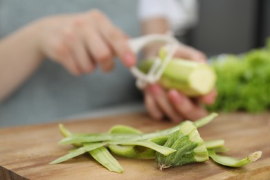 Photo of Woman peeling fresh zucchini at table, focus on peels