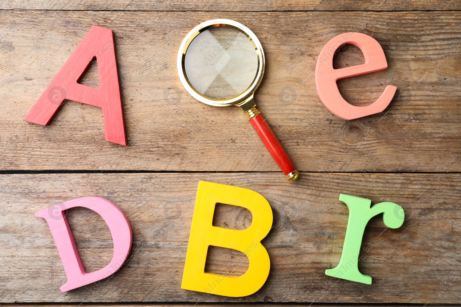 Photo of Different color letters and magnifier glass on wooden background, flat lay. Find keywords concept