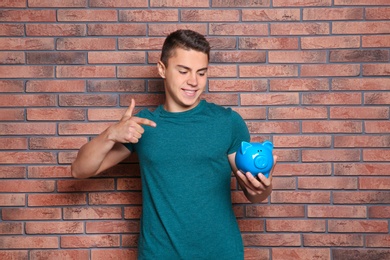 Photo of Teenage boy with piggy bank near brick wall