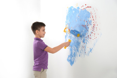 Photo of Little child painting wall with roller brush indoors