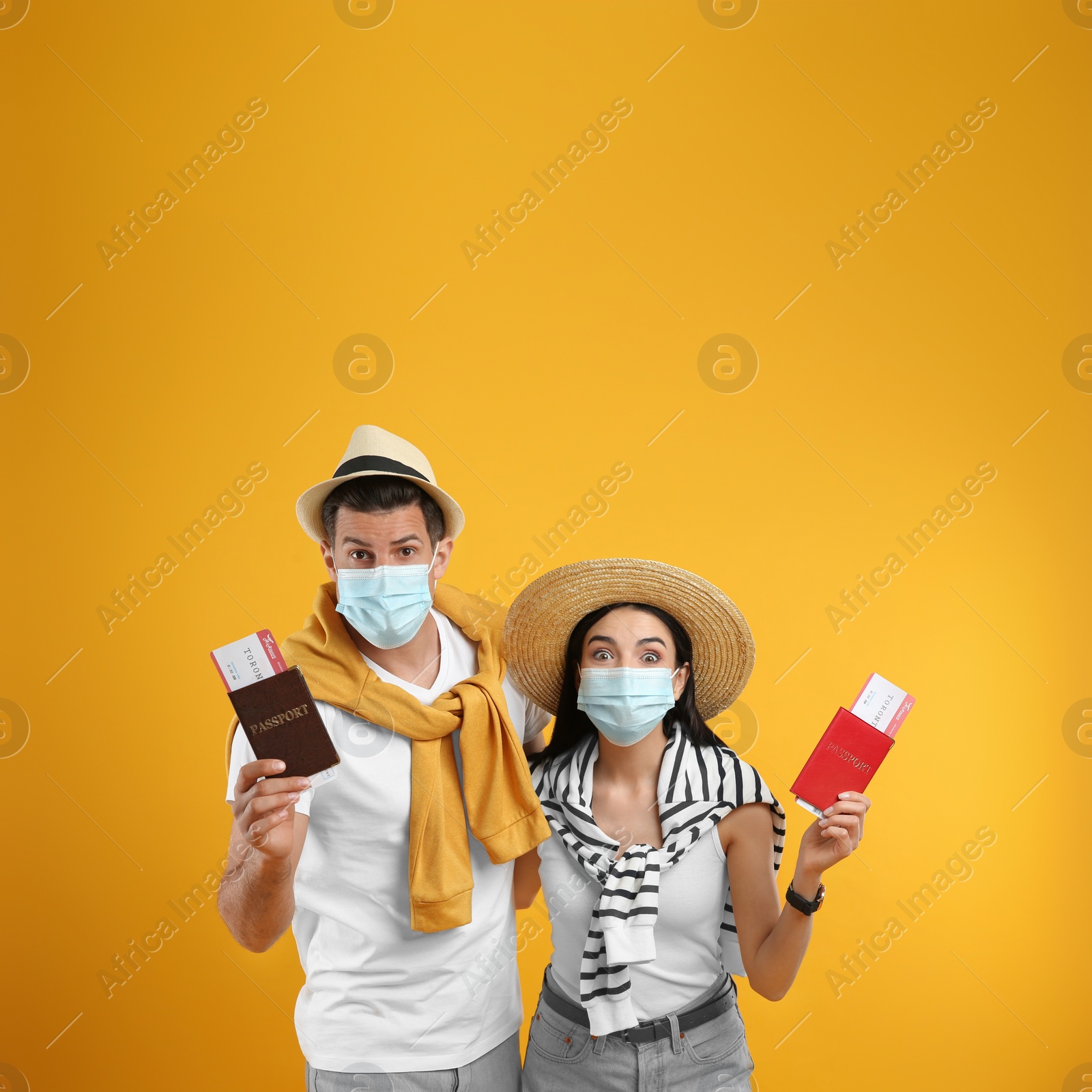 Photo of Couple of tourists in medical masks with tickets and passports on yellow background. Travelling during coronavirus pandemic