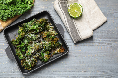 Photo of Tasty baked kale chips on light grey wooden table, flat lay