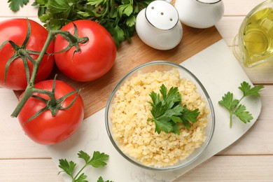 Photo of Delicious bulgur with parsley in bowl, tomatoes, oil and spices on table, flat lay