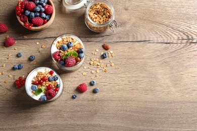 Tasty dessert with yogurt, berries and granola on wooden table, flat lay. Space for text 