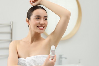 Beautiful young woman applying deodorant in bathroom