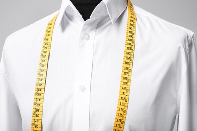 Photo of White shirt with tailor's measuring tape on mannequin against grey background, closeup