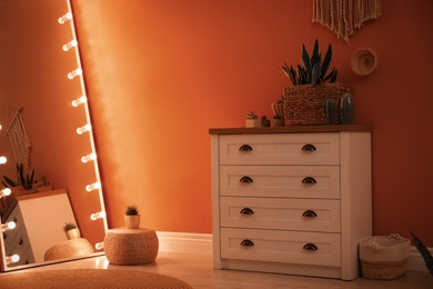 Large mirror with light bulbs and chest of drawers in stylish room interior