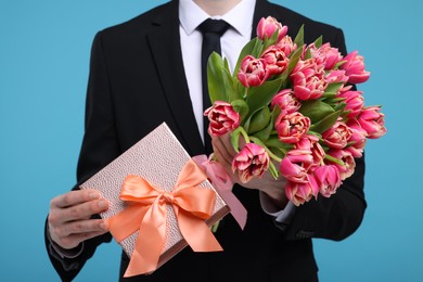 Photo of Man with beautiful bouquet and present on light blue background, closeup