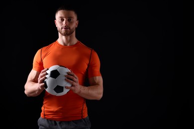 Photo of Athletic young man with soccer ball on black background. Space for text