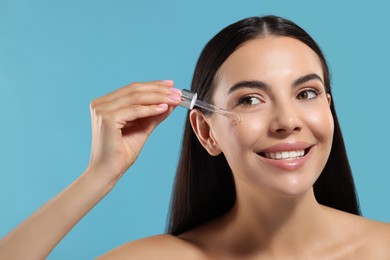 Photo of Beautiful young woman applying serum onto her face on light blue background