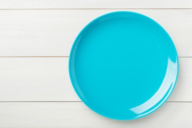 Photo of Empty light blue ceramic plate on white wooden table, top view. Space for text