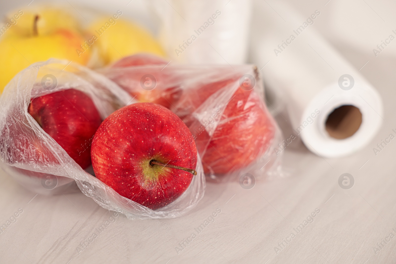 Photo of Plastic bag with fresh apples on white table, closeup