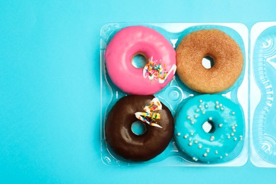 Box of delicious donuts on light blue background, top view. Space for text