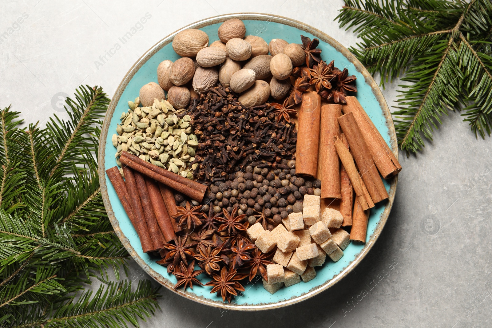 Photo of Different spices with nuts in bowl and fir branches on light gray textured table, flat lay