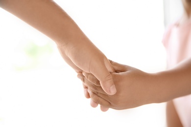 Children holding hands on light background, closeup. Unity concept