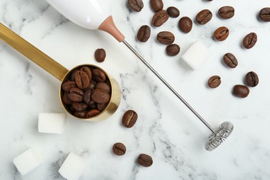 Milk frother wand, sugar cubes and coffee beans on white marble table, flat lay