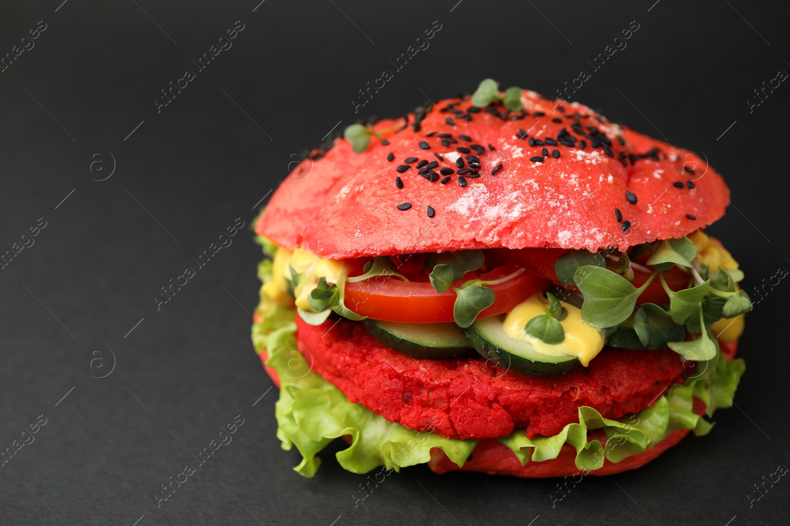 Photo of Tasty pink vegan burger with vegetables, patty and microgreens on black background, closeup. Space for text