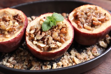 Tasty baked apples with nuts, honey and mint in baking dish on table, closeup