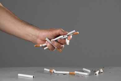 Stop smoking concept. Man holding cigarettes above gray table, closeup